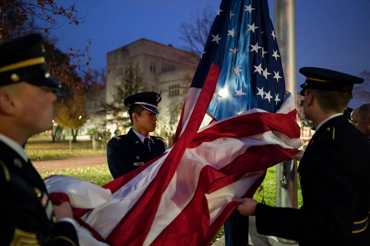 Students in military uniform raising an American flag.